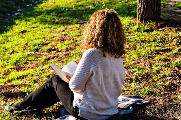 Femme aux cheveux blonds et bouclés lisant dans le parc.