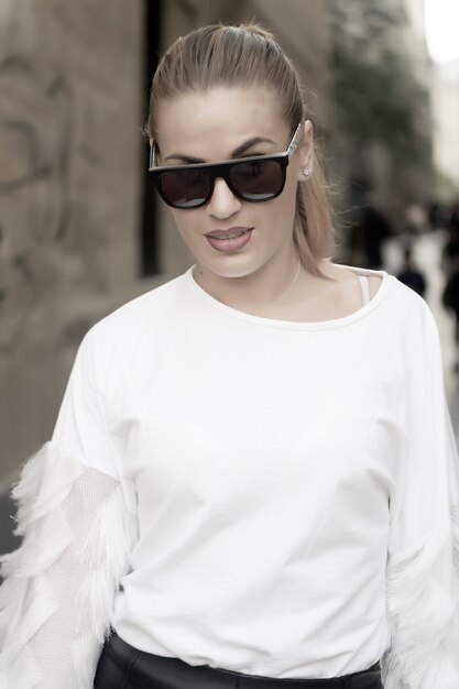 Femme aux cheveux blonds en chemisier blanc lunettes de soleil à pied à paris france mode beauté style