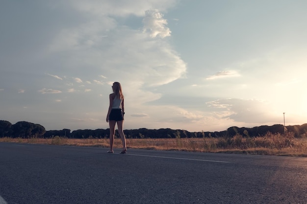 Femme aux cheveux blonds marchant sur la route au coucher du soleil en short