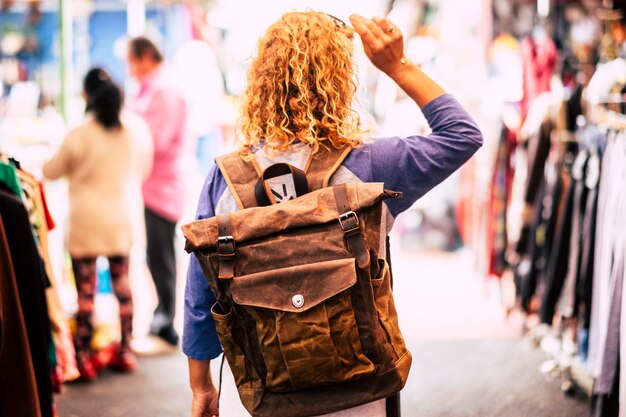 Femme Aux Cheveux Bouclés Blonds Backpacker Traveler Vu De L'arrière Au Marché D'occasion Profitant Du Shopping Et Des Vacances Alternatives