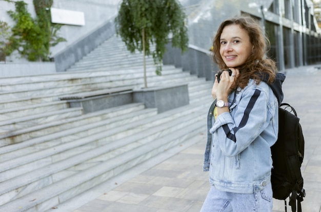 Femme aux cheveux bouclés charismatique Portet en veste en jean avec sac à dos et casque à l'extérieur en ville