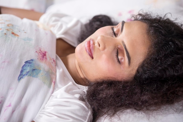 Photo une femme aux cheveux bouclés dort bien sur le lit.