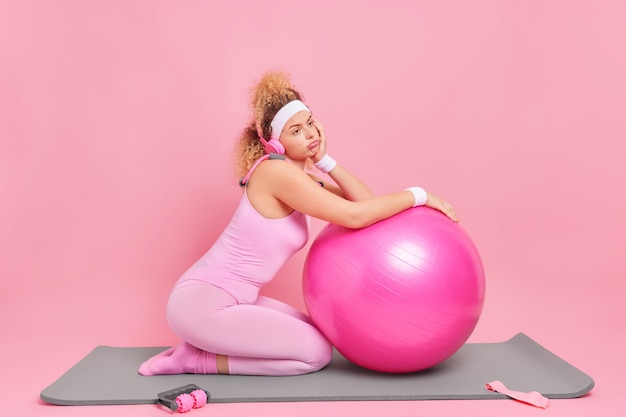 Une femme aux cheveux bouclés mécontente se sent fatiguée après un entraînement de fitness s'appuie sur un ballon suisse