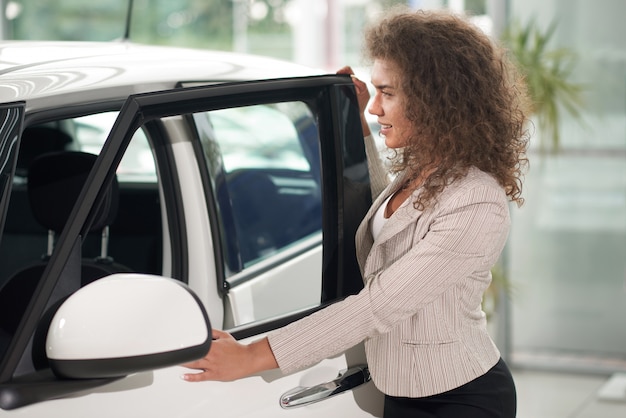 Femme aux cheveux bouclés ouvrant la porte de la voiture blanche.