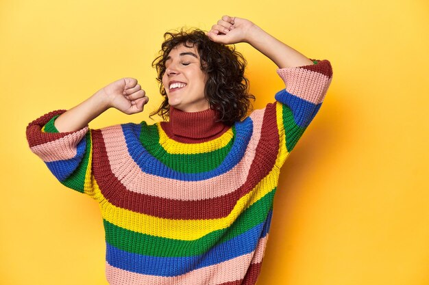 Photo une femme aux cheveux bouclés en sweat-shirt multicolore célébrant un jour spécial saute et lève les bras