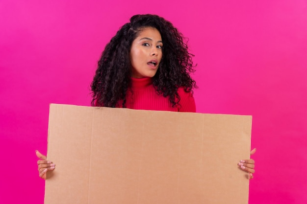 Femme aux cheveux bouclés tenant une pancarte sur un fond rose tourné en studio