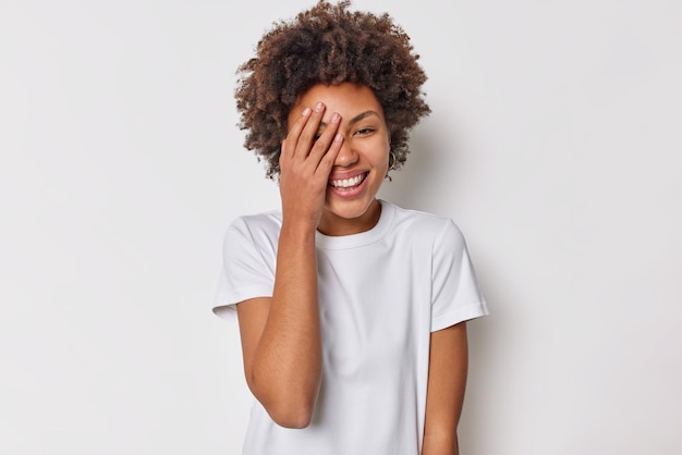 une femme aux cheveux bouclés et touffus fait que le visage de la paume se sent joyeux de rire devant quelque chose habillé avec désinvolture contre le blanc. Émotions des gens et concept de sentiments sincères