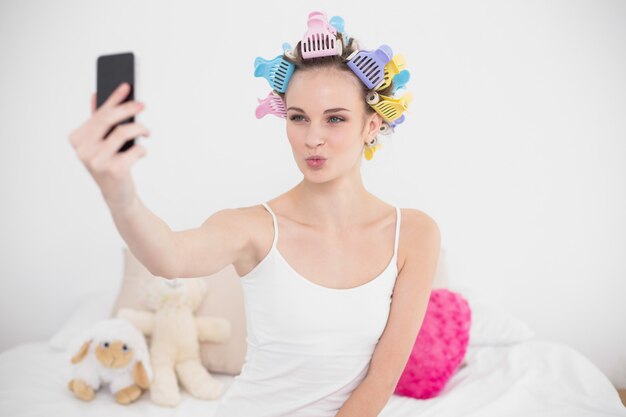 Femme aux cheveux brune naturelle dans des bigoudis prenant une photo d&#39;elle-même avec téléphone portable