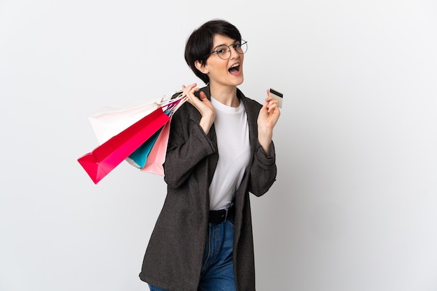 Femme aux cheveux courts sur un espace isolé tenant des sacs à provisions et une carte de crédit