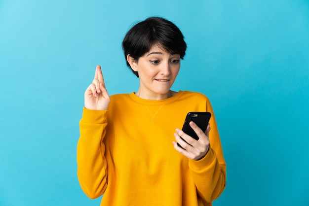 Femme aux cheveux courts sur fond isolé à l'aide de téléphone mobile avec les doigts traversant