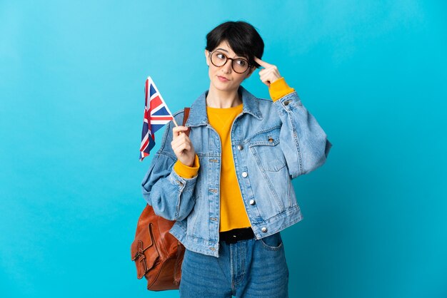 Femme aux cheveux courts tenant un drapeau du Royaume-Uni isolé sur l'espace bleu ayant des doutes et de la pensée