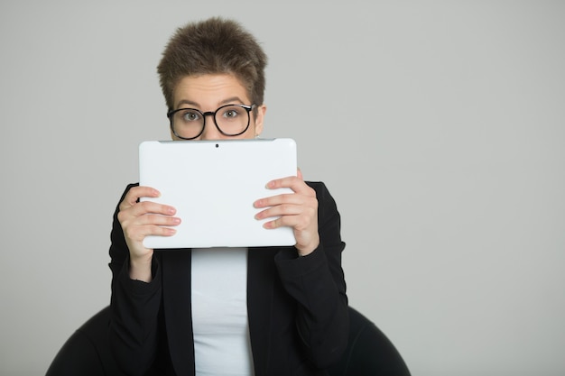 Femme aux cheveux courts sur la tête, dans un costume et des lunettes avec une tablette dans ses mains à l'image d'un homme