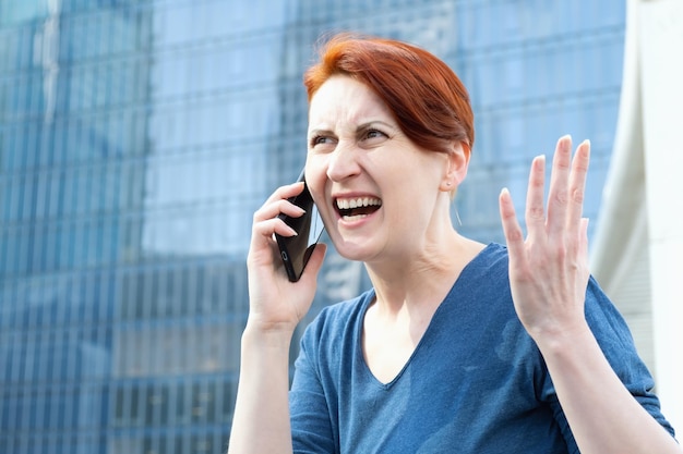 Une femme aux cheveux courts tient un smartphone et crie furieusement dans le microphone