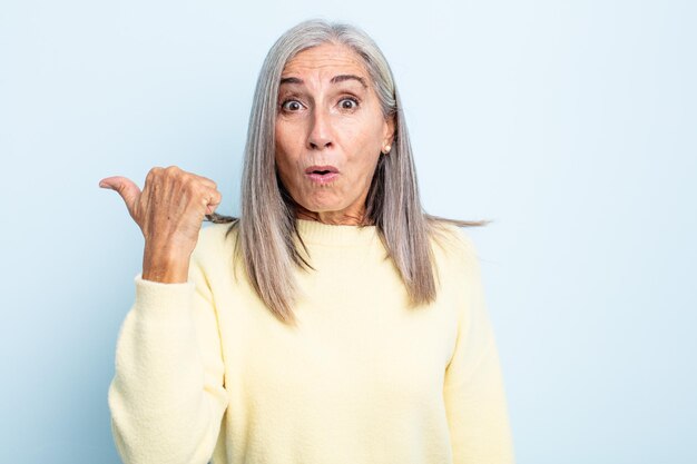 Femme aux cheveux gris d'âge moyen ayant l'air étonnée d'incrédulité, pointant l'objet sur le côté et disant wow, incroyable