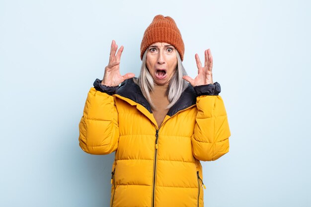 Femme aux cheveux gris d'âge moyen criant avec les mains en l'air. concept de temps froid