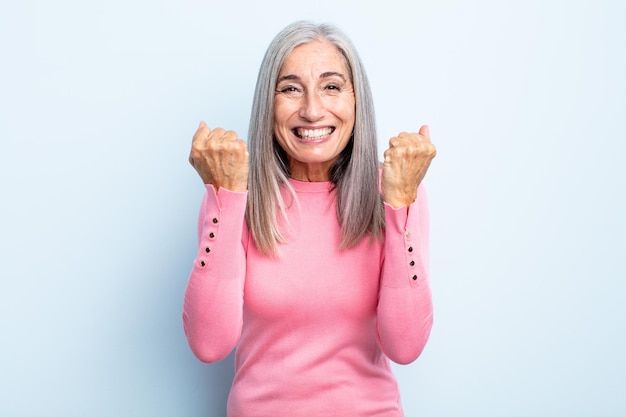 Femme aux cheveux gris d'âge moyen criant triomphalement, riant et se sentant heureuse et excitée tout en célébrant le succès