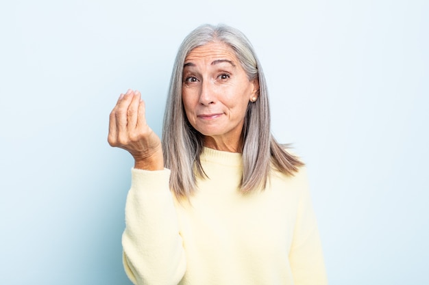 Femme aux cheveux gris d'âge moyen faisant un geste de capice ou d'argent, vous disant de payer vos dettes !