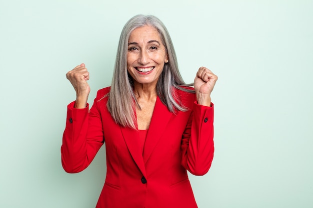 Femme aux cheveux gris d'âge moyen se sentant choquée, riant et célébrant le succès. concept de femme d'affaires senior