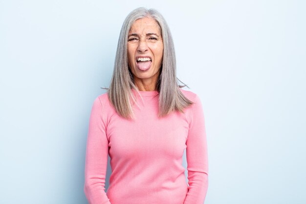 Femme aux cheveux gris d'âge moyen se sentant dégoûtée et irritée tirant la langue n'aimant pas quelque chose de méchant et de dégoûtant