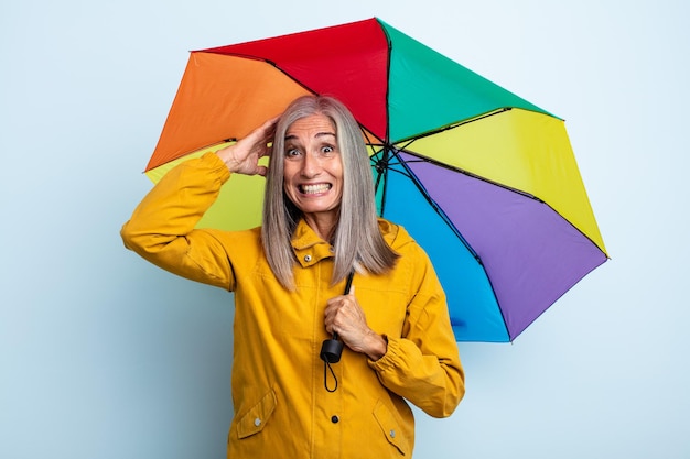 Femme aux cheveux gris d'âge moyen se sentant stressée, anxieuse ou effrayée, les mains sur la tête. concept parapluie et pluie
