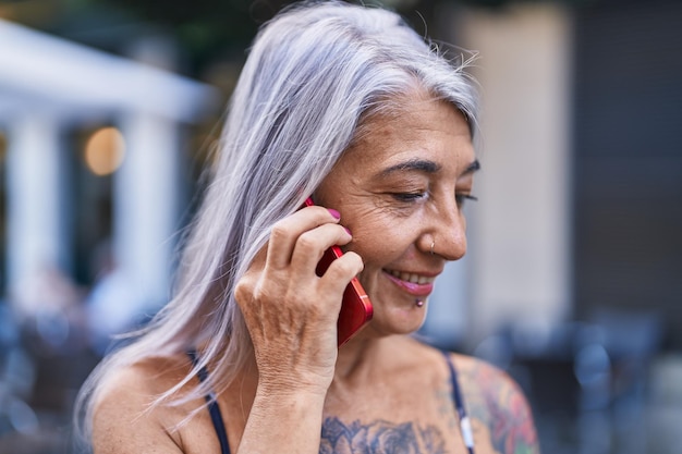 Femme aux cheveux gris d'âge moyen souriant confiant parlant sur le smartphone dans la rue