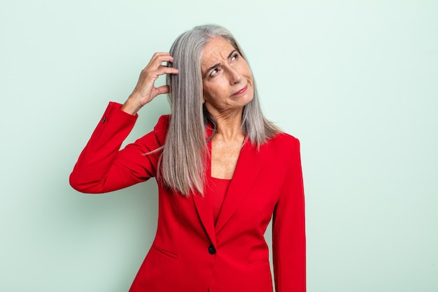 Femme aux cheveux gris d'âge moyen souriant joyeusement et rêvassant ou doutant. concept de femme d'affaires senior