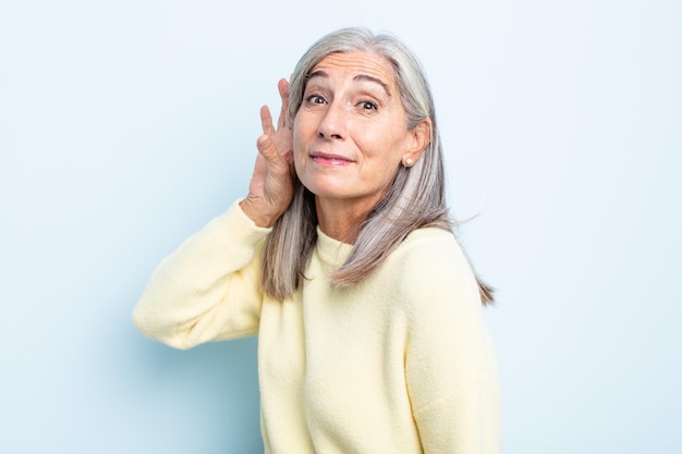 Femme aux cheveux gris d'âge moyen souriant, regardant curieusement sur le côté, essayant d'écouter les commérages ou d'entendre un secret