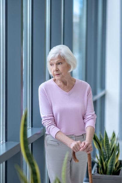 Femme aux cheveux gris avec un bâton de marche debout et à la réflexion