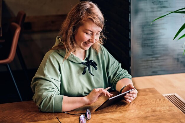 Une femme aux cheveux longs dessine sur une tablette et sourit à la table du café Mise au point sélective