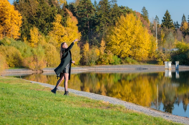 Une femme aux cheveux longs se promène dans un parc d'automne près d'un étang et jette des pierres dans l'eau