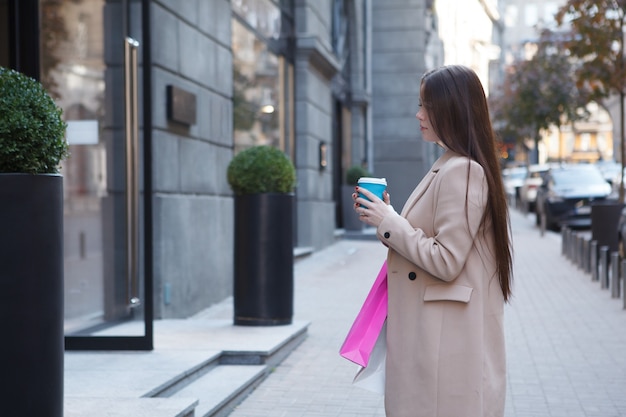 Femme aux cheveux longs tenant des sacs à provisions, regardant l'affichage au détail d'une boutique en centre-ville