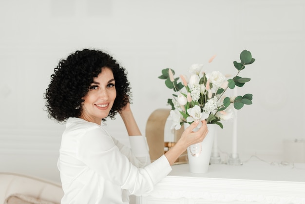 Femme aux cheveux noirs bouclés et un sourire blanc comme neige et touche un bouquet de fleurs