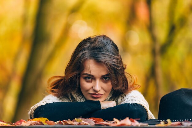 Une femme aux cheveux noirs gracieuse regarde la caméra et s’appuie tête par dessus sur la forêt en automne.