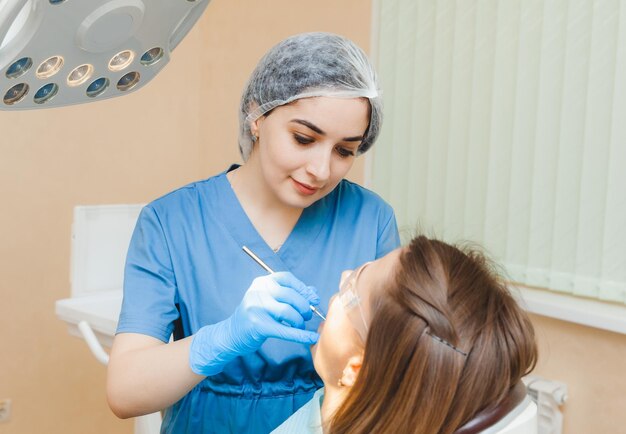 Une femme aux cheveux noirs positive est assise dans le cabinet du dentiste lors d'un examen par le dentiste examinant les dents de la femme