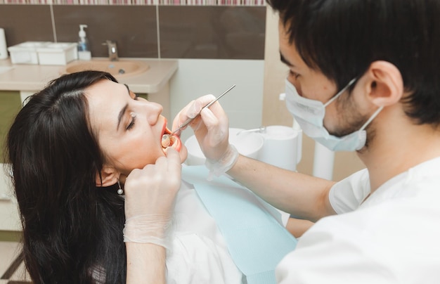 Une femme aux cheveux noirs positive est assise dans le cabinet du dentiste lors d'un examen par le dentiste examinant les dents de la femme