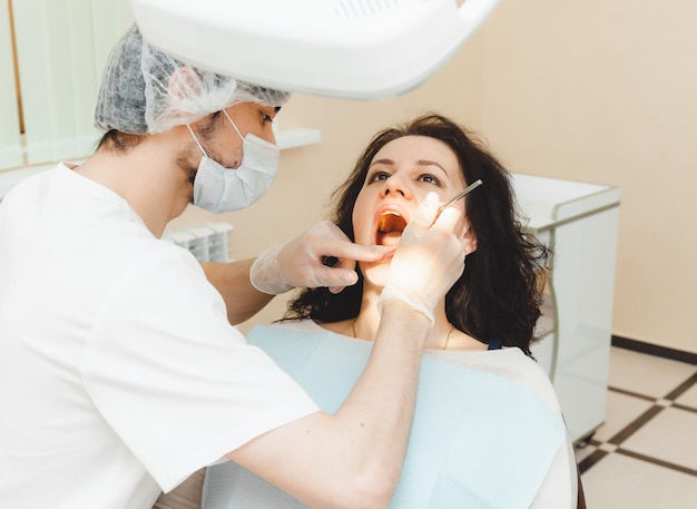 Une femme aux cheveux noirs positive est assise dans le cabinet du dentiste lors d'un examen par le dentiste examinant les dents de la femme