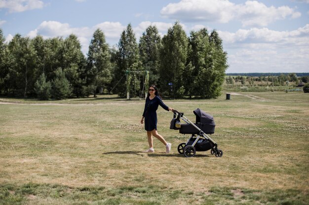 Femme aux cheveux noirs avec poussette dans le parc en été