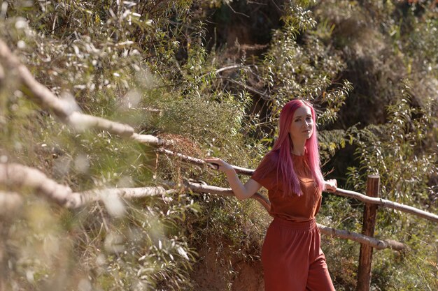 Photo une femme aux cheveux roses se tient près d'une clôture en bois dans la forêt et profite du soleil