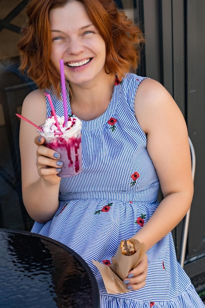 femme aux cheveux rouges dans un café boit un cocktail d'été, heureux, rit, sourit.