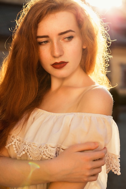 Femme aux cheveux rouges à la mode avec des épaules nues posant dans des rayons de soleil