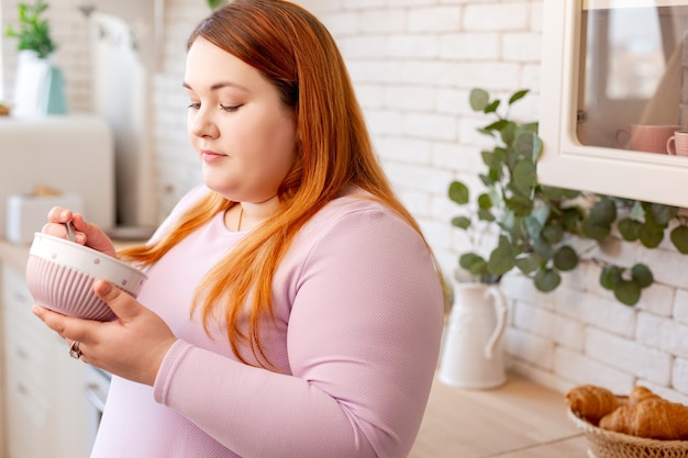 Femme aux cheveux rouges sérieuse regardant dans le bol tout en ayant toujours faim