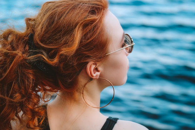 Une femme aux cheveux roux et au haut noir regarde l'eau.