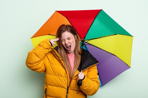 Femme aux cheveux roux à la recherche d'un geste de suicide malheureux et stressé faisant un concept de parapluie de signe d'arme à feu