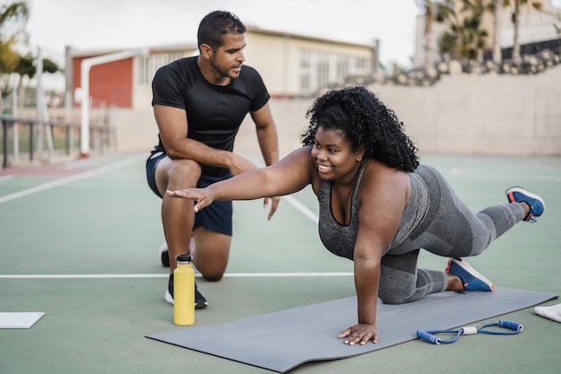 Femme aux courbes africaines et entraîneur personnel faisant une séance d'entraînement de pilates en plein air - Accent principal sur le visage de la fille