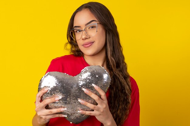 une femme aux longs cheveux bouclés portant des lunettes et tenant un cœur avec des pierres brillantes