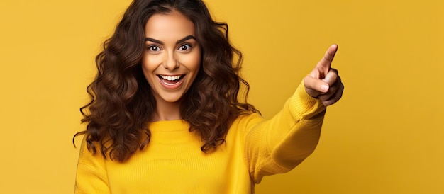 Femme aux longs cheveux bruns pointant avec enthousiasme recommandant le concept publicitaire sur fond jaune isolé