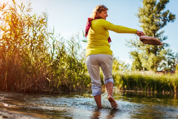 Femme aux pieds nus d'âge moyen marchant sur la rive du fleuve le jour du printemps. Dame âgée s'amusant dans la forêt en profitant de la nature.