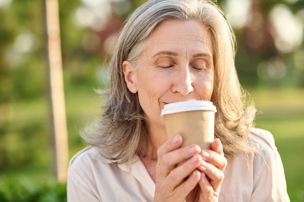 Femme aux yeux fermés tenant un verre de café