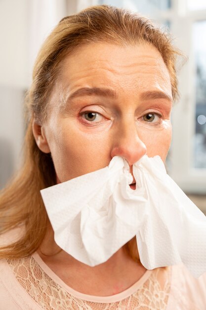 Femme aux yeux verts allergique ayant une serviette dans le nez tout en éternuant toute la journée