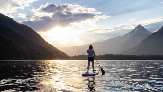 Une femme aventureuse fait du paddle dans un lac autour d'un paysage de montagnes canadiennes